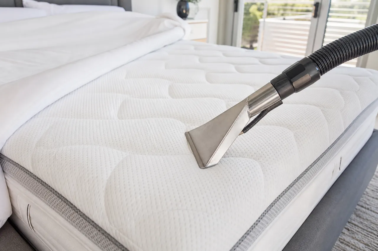 Upholstery tool freshening the surface of a mattress in a bright bedroom